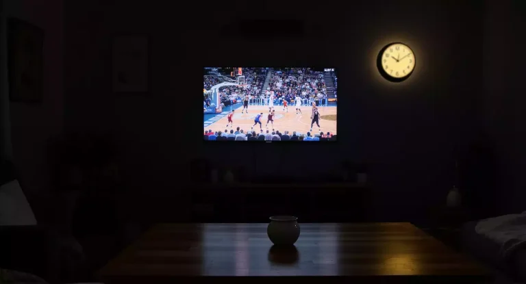 Donkere woonkamer met basketbalwedstrijd op de televisie en een wandklok die laat op de avond aangeeft